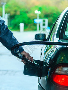 男子在加油站用煤气或汽重新装满车在户外持有燃料泵背景图片