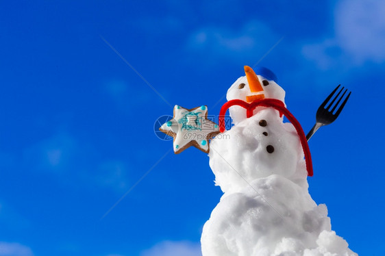 圣诞小雪人穿着蓝螺丝顶的戴着帽子红围巾外出有叉姜饼蛋糕干明星冬季节特制蓝天空背景图片