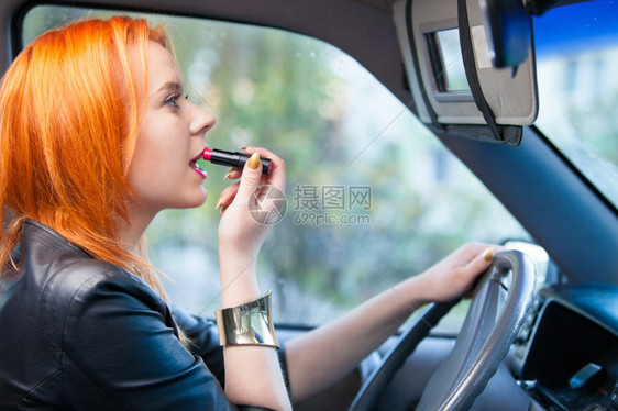 年轻女司机红发少在开车时嘴唇上涂油图片
