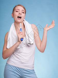 年轻有趣的女孩唱歌给牙刷她的白在蓝色上玩耍每日牙科护理工作室拍摄图片