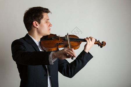 年轻优雅的小提琴家手在灰色上拉小提琴古典音乐演播室拍摄图片
