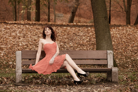 穿着红裙子的全长时装女青年户外放松坐在公园里长的椅上图片