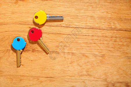 木制表格背景上三把有多彩塑料外衣盖的家用钥匙图片
