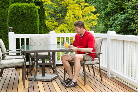 成年男子的横向照片他拿着一杯橙汁同时准备在户外院子上用全季节盛开的绿树和黄阅读一本杂志图片