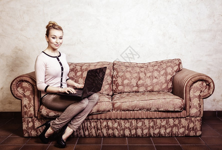 技术互联网现代生活方式概念使用笔记本电脑在回放沙发上工作的全时年轻商业妇女或学生室内旧照片图片
