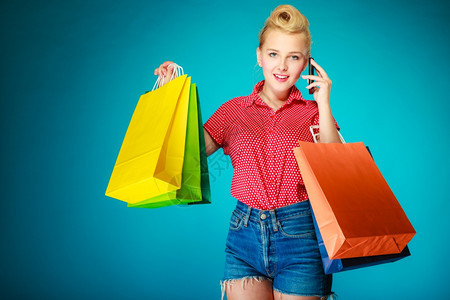 Pinup女孩穿旧型的年轻女子买衣服打手机客户拿着鲜艳的蓝色购物袋零售和销图片