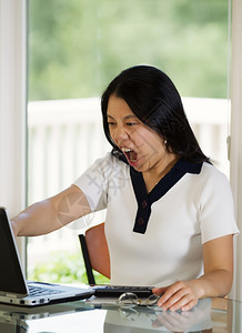成年女在家工作时计算机屏幕上愤怒地显露在她身上的垂直图像图片