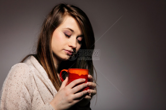 一位美丽的caucasian女人的近身拿着一杯漂亮的红温暖饮料灰色背景图片