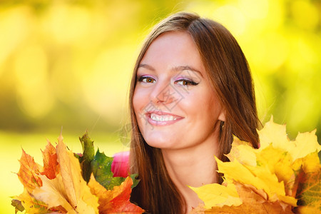 秋天季节快乐的年轻女孩肖像在秋天公园森林里拿着丰富多彩的叶子图片