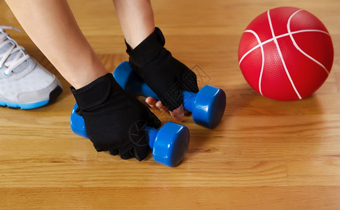 横向形象女双手在背着红球和鞋的木制健身地板上举起小重量时戴运动手套同时身穿运动手套用红球和鞋从木制健身地板上举起小重量图片