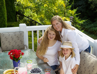 成年母亲眼前视线显示她有两个幸福的女儿在外边吃早餐时在夏季的露天吃早餐在有背景的树林院子上图片