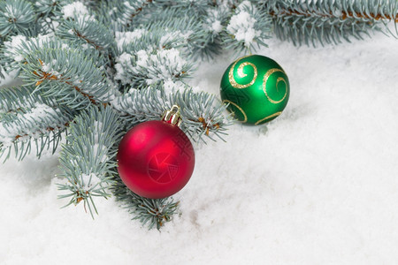 红色和绿的圣诞装饰品挂在雪上真正的蓝色斯普鲁树枝上图片