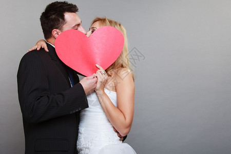 结婚日金发新娘和郎快乐吻红心灰色背景图片