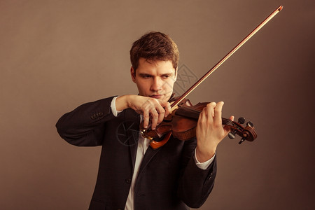 年轻优雅的小提琴家手在棕色古典音乐演播室拍小提琴图片