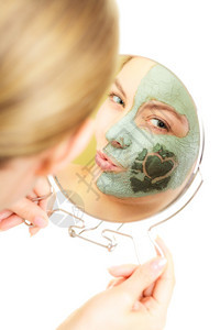 穿着泥土面具的女人脸部和看着镜子在白色上吹一个吻美容治疗图片