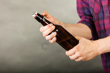 青年男子在灰色背景上拿着啤酒瓶图片