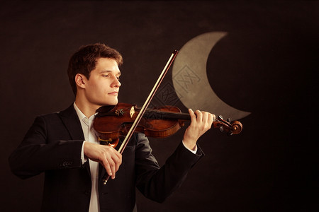 年轻可爱的小提琴家手在月夜拉小提琴古典音乐工作室拍图片