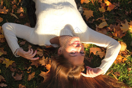 年轻女孩秋天躺落叶手下黄色的紫女孩花园背景图片