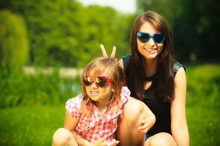 夏天母亲的肖像女儿戴着墨镜坐在草原上或公园里图片