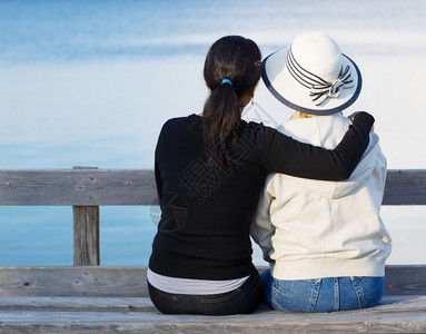 母亲和成年女儿紧地坐在木椅上看湖图片