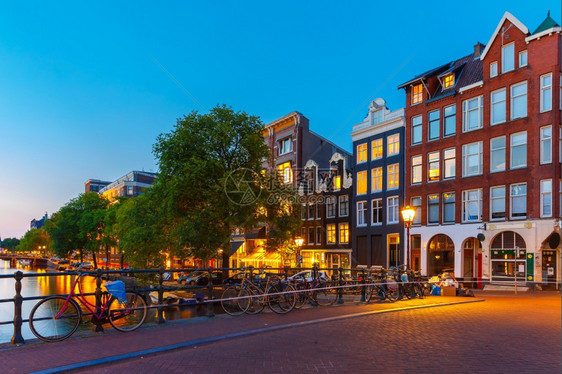 荷兰阿姆斯特丹运河桥梁和典型房屋船只和自行车的夜间城市景象图片