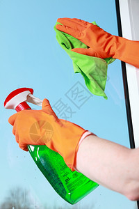 用绿色抹布和喷洒洗涤剂用橙色手套清洗窗图片