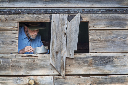 牛仔在旧小屋里做饭或吃东西脸朝窗子看得见图片