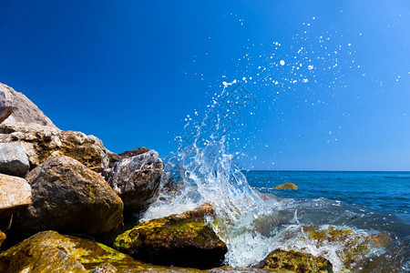 海浪在形成飞溅状的热带海滩上撞击岩石希腊桑托里尼图片