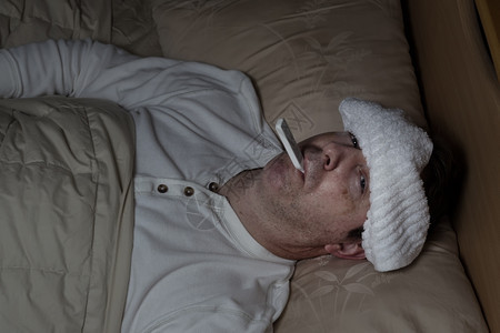 成年男子的横向形象前额有湿毛巾躺在床上测试体温图片