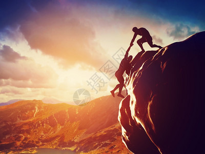 攀爬在岩石上日落时山其中一人伸出手帮助攀爬在危险情况下帮助支持援背景图片