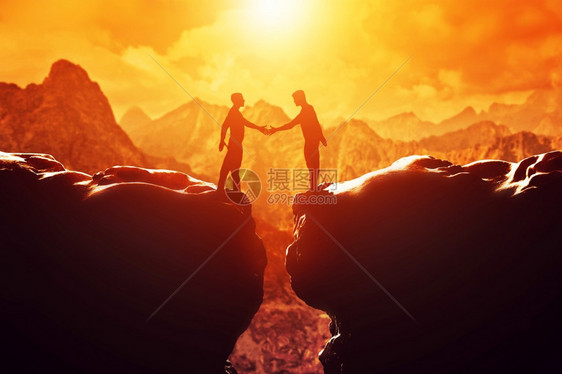 两个男人在日落时两座岩石山之间握手商业交易握手连接概念图片