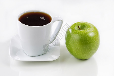 靠近一个纯净的绿苹果在软白桌上用光反射照的一杯咖啡新鲜黑焦点放在对象的前顶图片