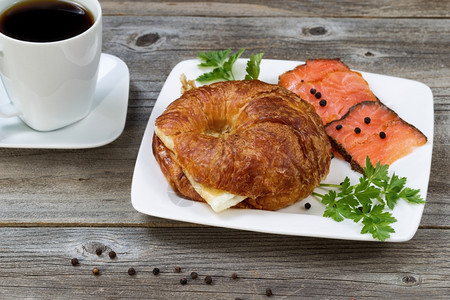最接近的早餐包括新鲜烤面鸡蛋冷烟鲑鱼正对面的欧斯利和在生锈木板上的黑咖啡关注牛角面包的前端和背景咖啡鲑鱼图片