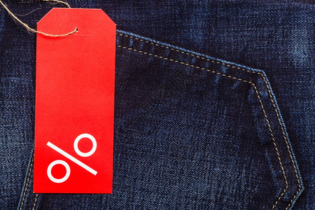 购买和销售概念在海军蓝牛仔裤口袋服棉料背景上以百分数符号和复制空间进行贴合的红标签图片