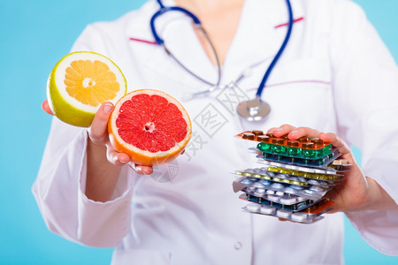 健康与均衡饮食概念在两种维他命来源药丸或水果之间做出选择医生提供化学和天然维他命持有一堆药和蓝葡萄园图片