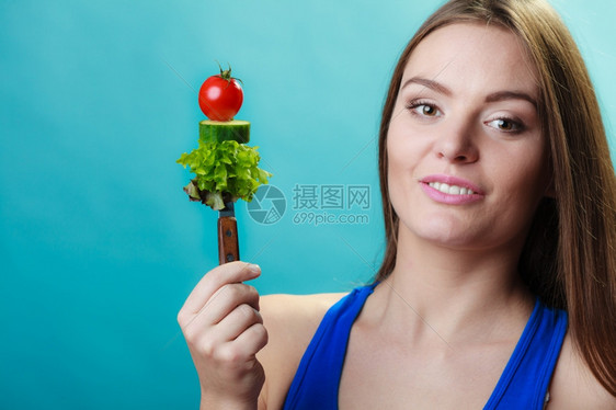 健美体重减肥概念手持蓝底鲜混合蔬菜叉子的运动女健身图片