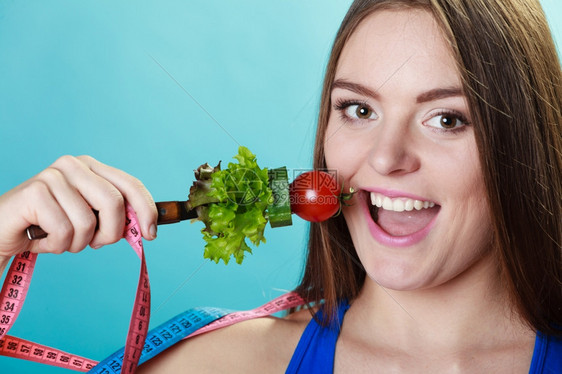 健美体重减肥概念运动健壮的女身子用新鲜混合蔬菜和蓝底胶带作为叉子和计量胶带图片