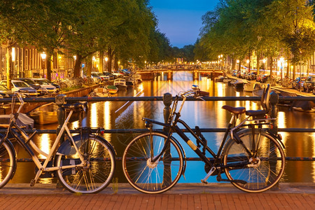 荷兰阿姆斯特丹运河和带有典型荷兰码头房屋船只和自行车的桥梁夜间照明图片