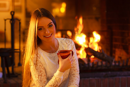 在家的冬天暖气女人笑的长发郎在壁炉放暖拿着杯子和热饮图片