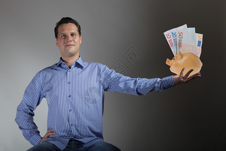 有猪银行和欧元钞票灰色背景的快乐男人图片