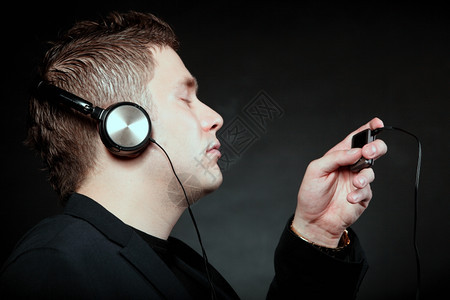 有耳机的年轻男青学生使用mp3播放器听音乐眼睛闭着黑手背面图片