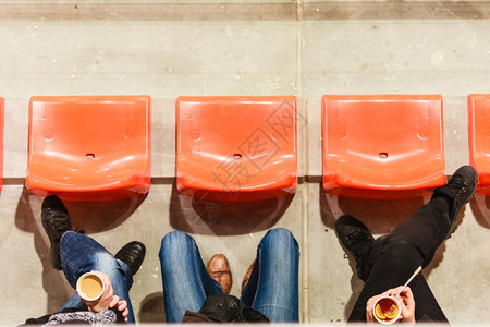 体育比赛娱乐和放松足球场的一排塑料椅和人腿手拿茶咖啡的一次热饮杯图片