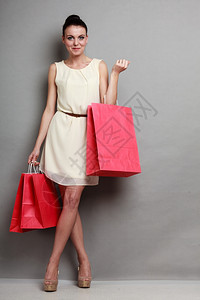 时装女郎穿着优雅的白色裙子手拿着红色购物袋灰背景工作室拍摄图片