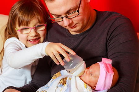 父亲和女儿在家沙发上用奶瓶喂养新生女婴图片