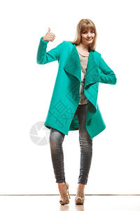 时装全长的快乐妇女牛仔裤时流行的绿色蓝大衣用拇指举起手牌势图片