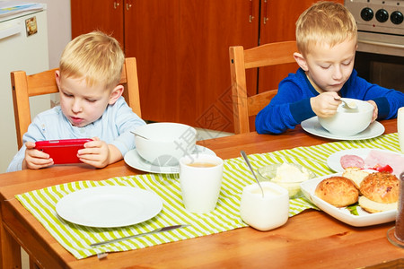 边吃边玩两位金发男孩子们在桌边吃早餐边玩手机背景
