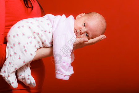 父母亲和爱的概念一个月大的女婴在母亲舒适怀抱红色背景图片