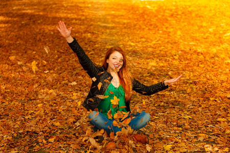 红发长女人在秋天的公园里向空中扔叶子图片