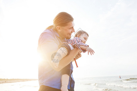 年轻父亲抱着孩子在海滩的空气中一起玩乐儿子和父母的关系图片素材