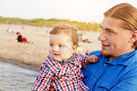 年轻父亲在海滩上抱着孩子玩得开心儿和父母的亲情图片